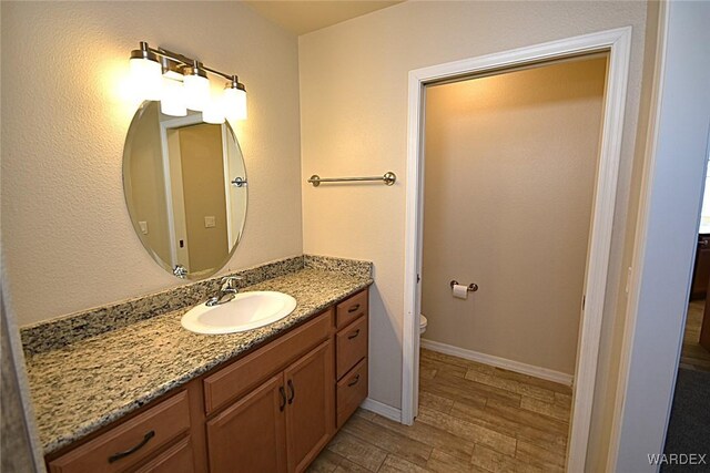 bathroom featuring baseboards, vanity, toilet, and wood finished floors