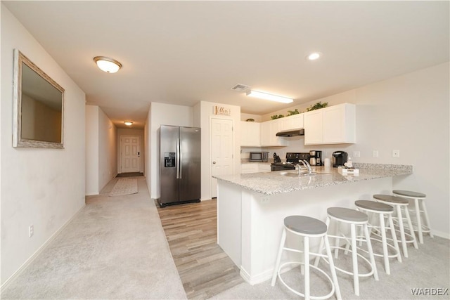 kitchen featuring a breakfast bar, a peninsula, stainless steel appliances, under cabinet range hood, and a sink