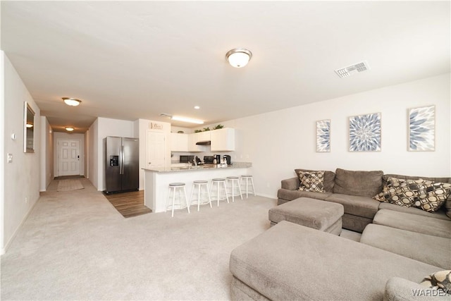 living area featuring light colored carpet, visible vents, and baseboards