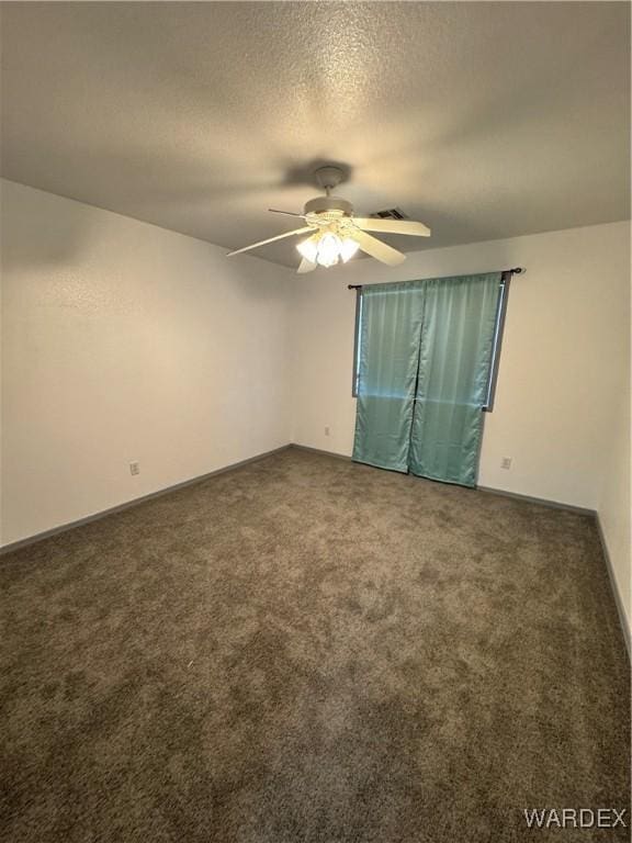 spare room with a ceiling fan, visible vents, dark carpet, and a textured ceiling