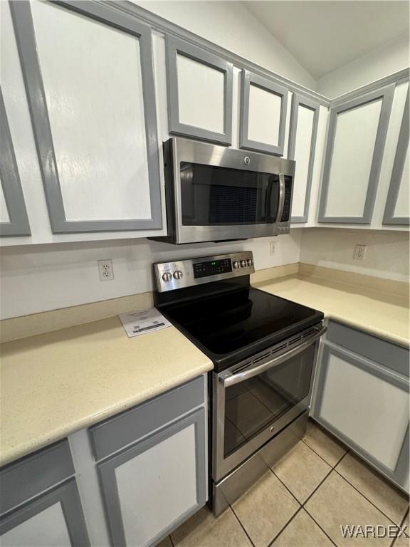 kitchen featuring vaulted ceiling, gray cabinets, stainless steel appliances, light countertops, and light tile patterned flooring