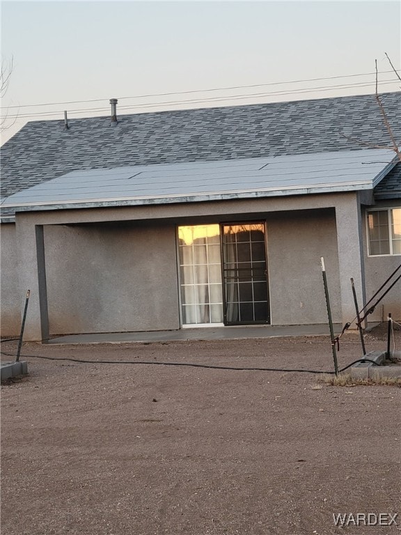 back of property at dusk featuring roof with shingles and stucco siding