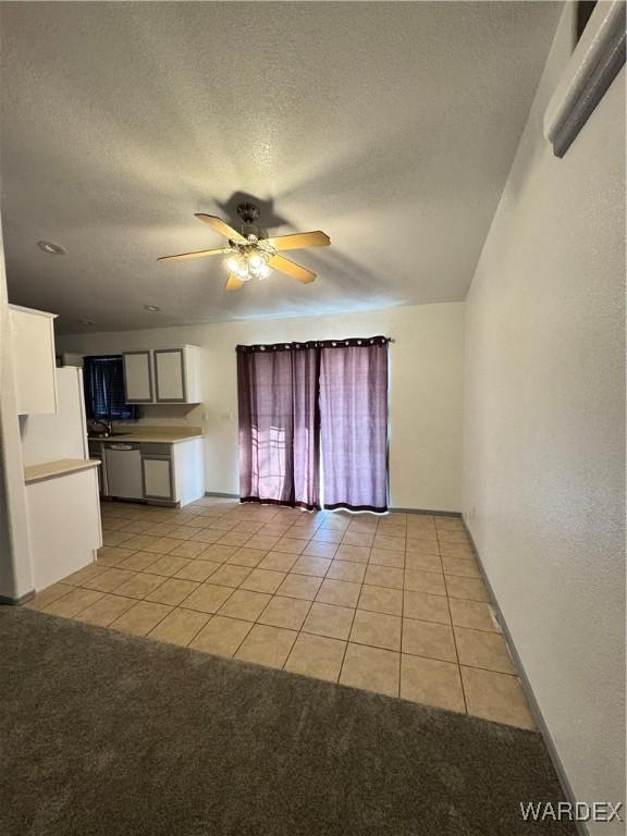 unfurnished living room featuring light tile patterned floors, ceiling fan, a textured ceiling, and light colored carpet