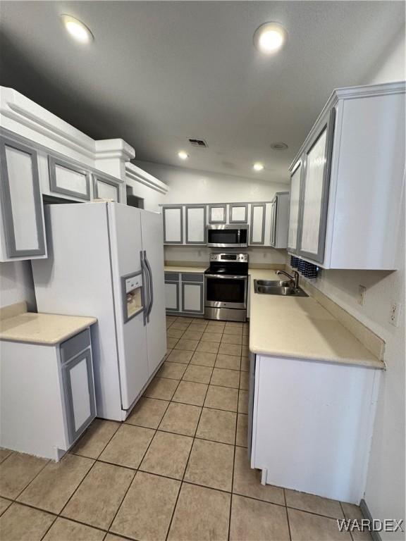 kitchen featuring light tile patterned floors, light countertops, appliances with stainless steel finishes, vaulted ceiling, and a sink