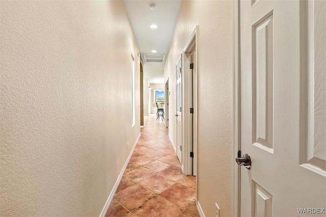 hallway featuring light tile patterned flooring, attic access, baseboards, and a textured wall