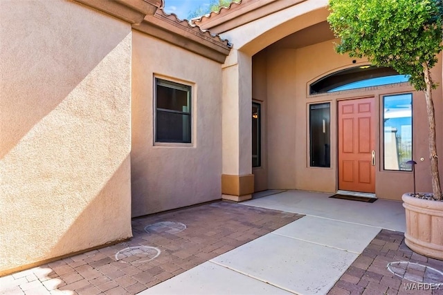 view of exterior entry with a tile roof, a patio area, and stucco siding