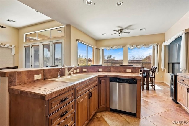 kitchen with visible vents, a ceiling fan, a sink, stainless steel dishwasher, and tile countertops