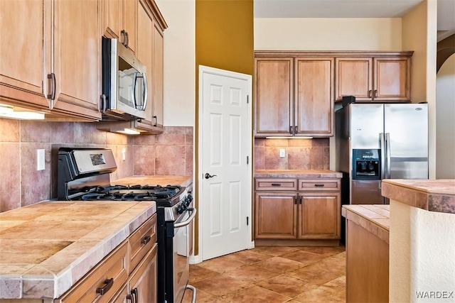 kitchen featuring light tile patterned floors, arched walkways, stainless steel appliances, decorative backsplash, and tile counters