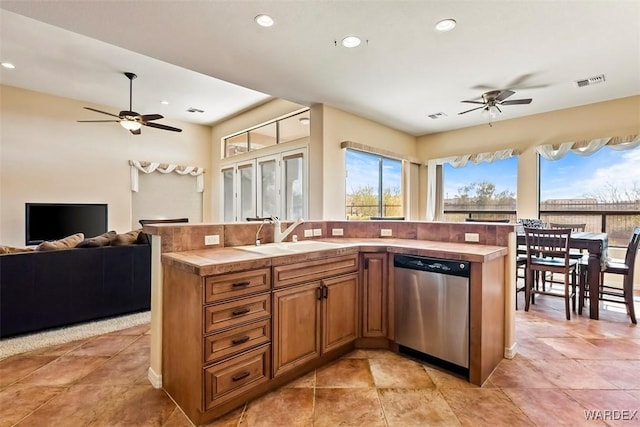 kitchen featuring tile counters, open floor plan, stainless steel dishwasher, a ceiling fan, and a sink