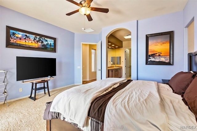 bedroom featuring baseboards, carpet floors, ensuite bathroom, arched walkways, and a ceiling fan