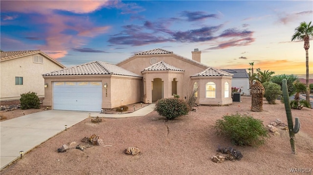 mediterranean / spanish house with an attached garage, concrete driveway, a tiled roof, stucco siding, and a chimney