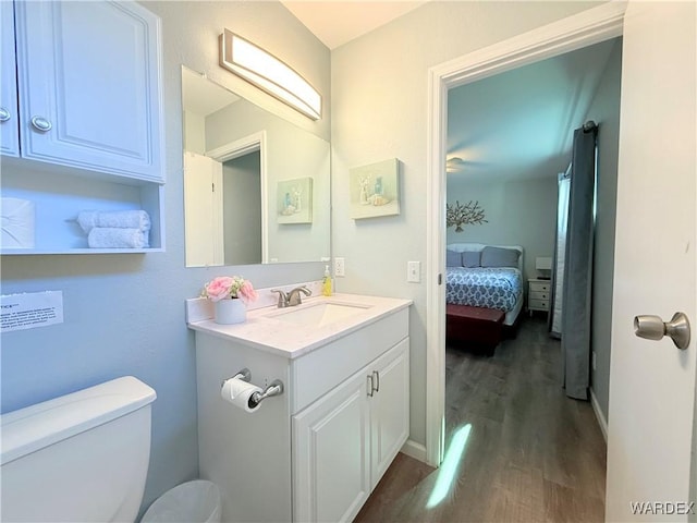 ensuite bathroom featuring toilet, connected bathroom, vanity, wood finished floors, and baseboards