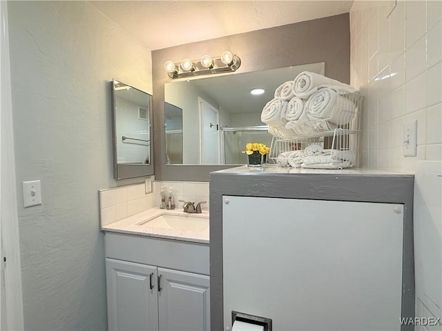 full bathroom with a shower, a textured wall, vanity, and decorative backsplash