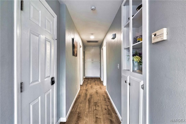 corridor featuring visible vents, baseboards, dark wood-style flooring, and a textured wall