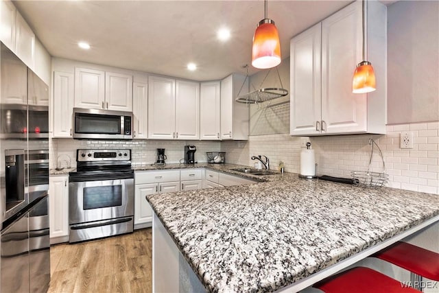 kitchen featuring stainless steel appliances, a peninsula, white cabinetry, and pendant lighting