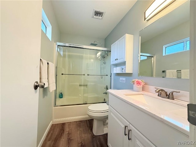 full bath featuring shower / bath combination with glass door, visible vents, toilet, vanity, and wood finished floors