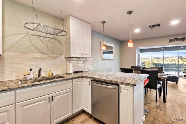 kitchen featuring a peninsula, light stone countertops, stainless steel dishwasher, white cabinetry, and a sink