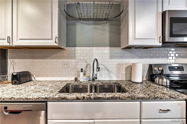 kitchen featuring stainless steel appliances, tasteful backsplash, white cabinets, a sink, and light stone countertops