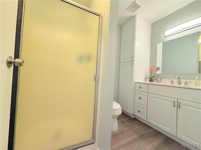 full bathroom featuring toilet, wood finished floors, vanity, visible vents, and a stall shower