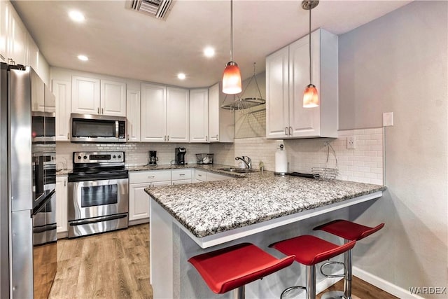 kitchen featuring visible vents, white cabinets, appliances with stainless steel finishes, a peninsula, and pendant lighting