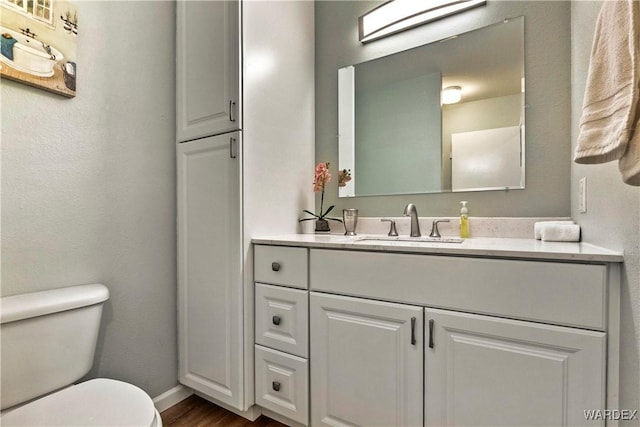 bathroom with toilet, wood finished floors, vanity, and baseboards