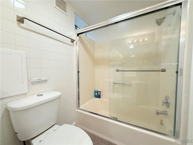 bathroom featuring visible vents, tile walls, toilet, and bath / shower combo with glass door