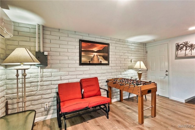 living area with brick wall, baseboards, and wood finished floors