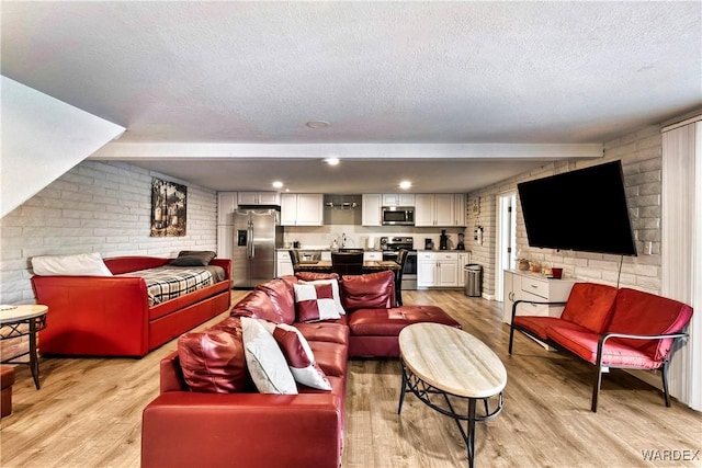 living room with brick wall, light wood-style flooring, and a textured ceiling