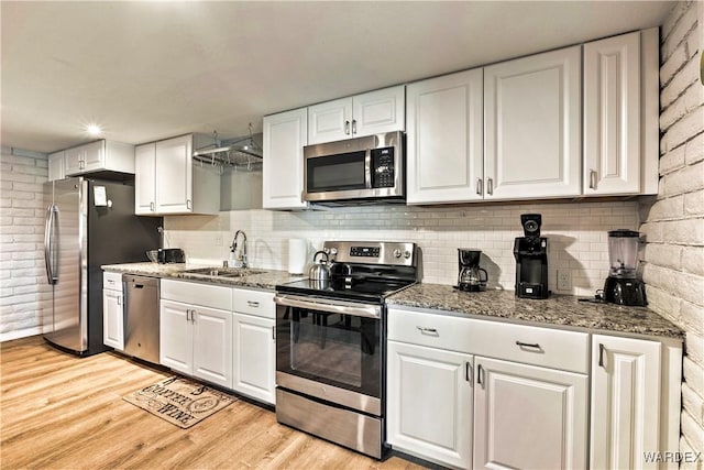 kitchen featuring white cabinets, dark stone countertops, stainless steel appliances, light wood-style floors, and a sink