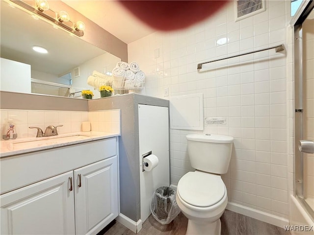 bathroom with toilet, wood finished floors, visible vents, vanity, and tile walls