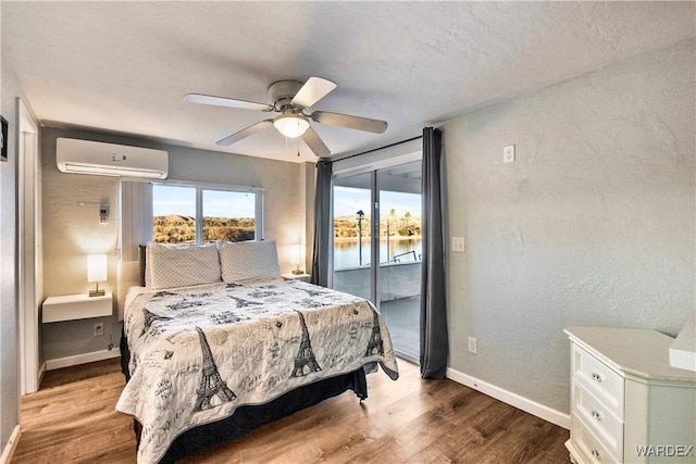 bedroom featuring a water view, access to exterior, a wall unit AC, and wood finished floors