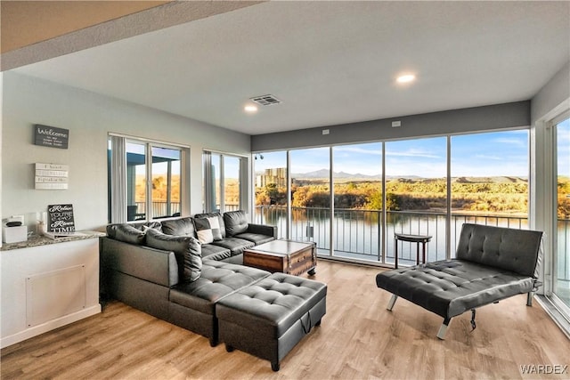 living room featuring light wood-style floors, visible vents, plenty of natural light, and a water and mountain view