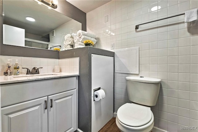 full bath with tile walls, toilet, wood finished floors, vanity, and backsplash