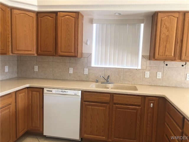 kitchen with brown cabinetry, dishwasher, a sink, and backsplash
