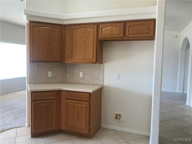 kitchen with baseboards, arched walkways, light countertops, brown cabinetry, and decorative backsplash
