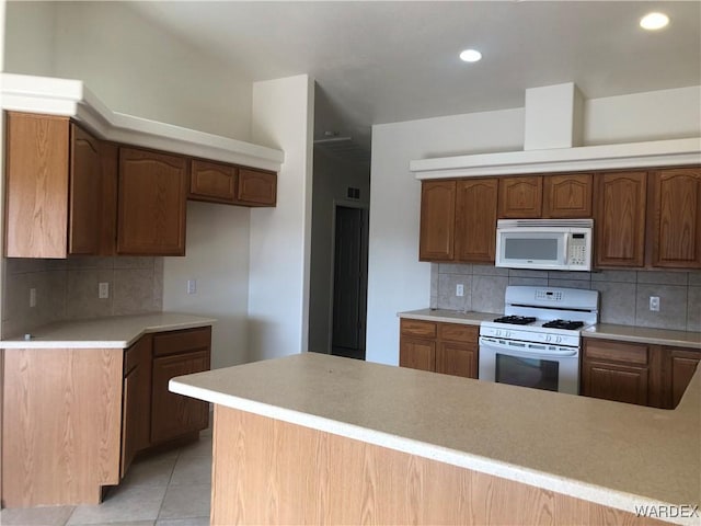 kitchen featuring light tile patterned floors, white appliances, a peninsula, light countertops, and backsplash