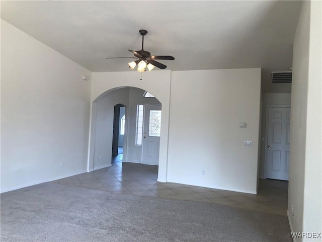 carpeted empty room with arched walkways, a ceiling fan, visible vents, and tile patterned floors