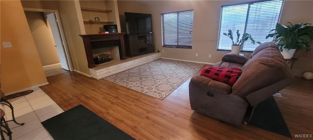 living area with baseboards, wood finished floors, and a fireplace with raised hearth