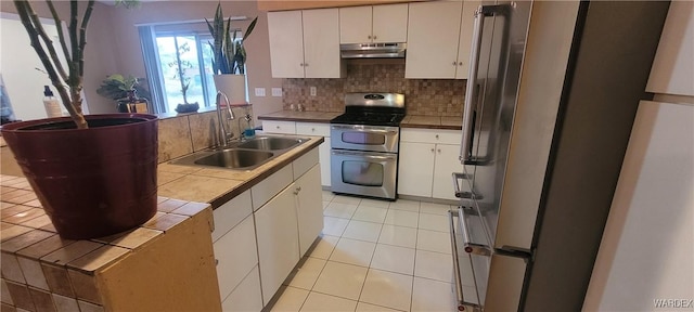 kitchen featuring tasteful backsplash, under cabinet range hood, tile countertops, stainless steel appliances, and a sink