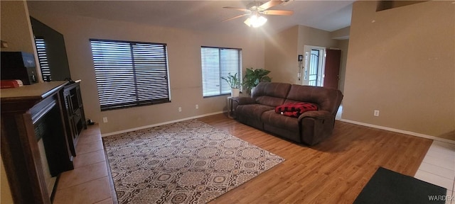 living area featuring baseboards, light wood finished floors, and ceiling fan