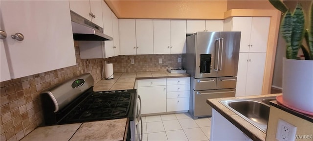 kitchen featuring under cabinet range hood, tasteful backsplash, white cabinetry, stainless steel appliances, and tile counters