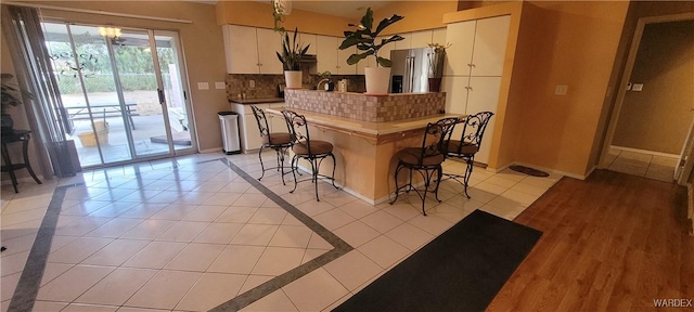 kitchen with a kitchen bar, tasteful backsplash, white cabinetry, stainless steel fridge, and baseboards