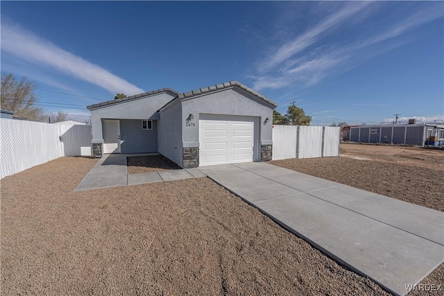 exterior space featuring stone siding, fence, an attached garage, and stucco siding