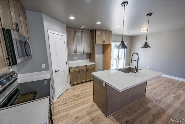 kitchen with light wood-style flooring, decorative light fixtures, a sink, appliances with stainless steel finishes, and a center island with sink