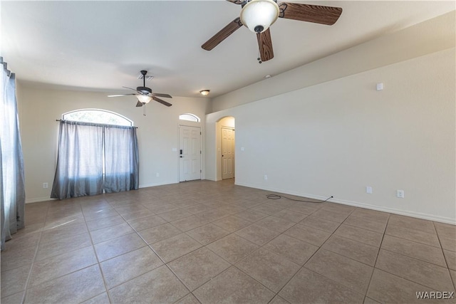 empty room featuring a ceiling fan, arched walkways, baseboards, and light tile patterned floors