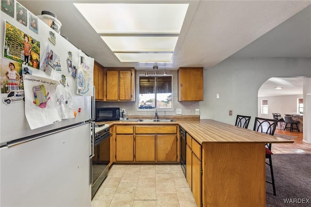 kitchen with a peninsula, a sink, a kitchen breakfast bar, black appliances, and brown cabinetry