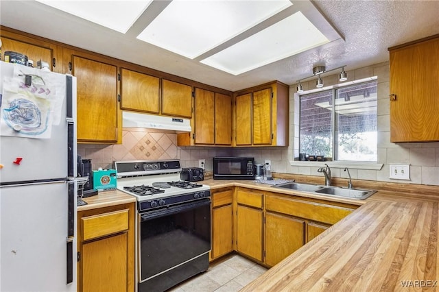 kitchen with freestanding refrigerator, under cabinet range hood, black microwave, a sink, and gas stove