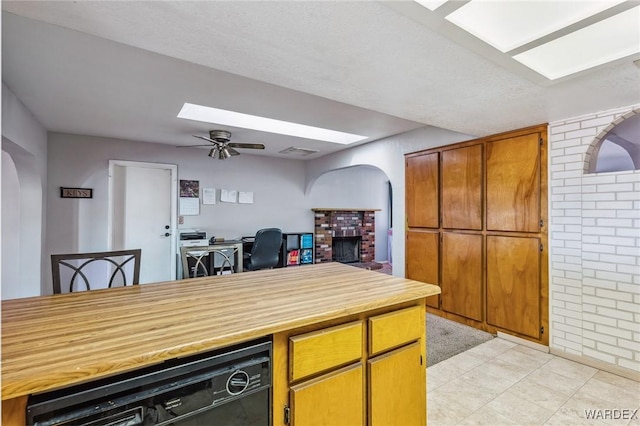 kitchen with ceiling fan, arched walkways, black dishwasher, light countertops, and brown cabinets