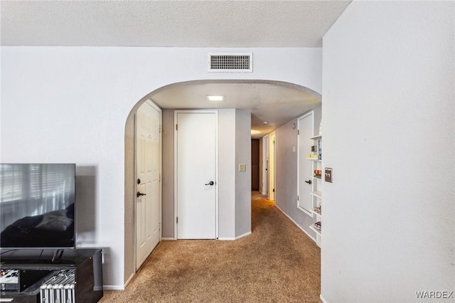 corridor featuring baseboards, visible vents, arched walkways, a textured ceiling, and carpet flooring