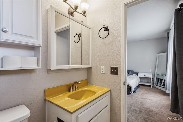 ensuite bathroom featuring toilet, a textured wall, connected bathroom, and vanity